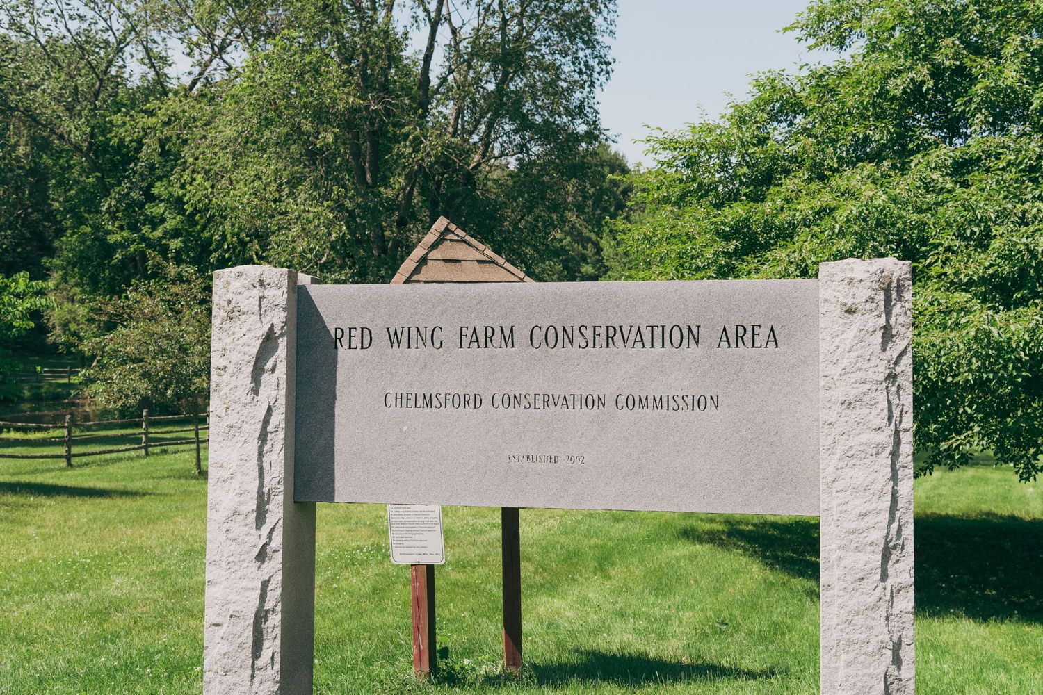 A stone sign marking the entrance to a farm conservation area stands in a grassy field with trees in the background.