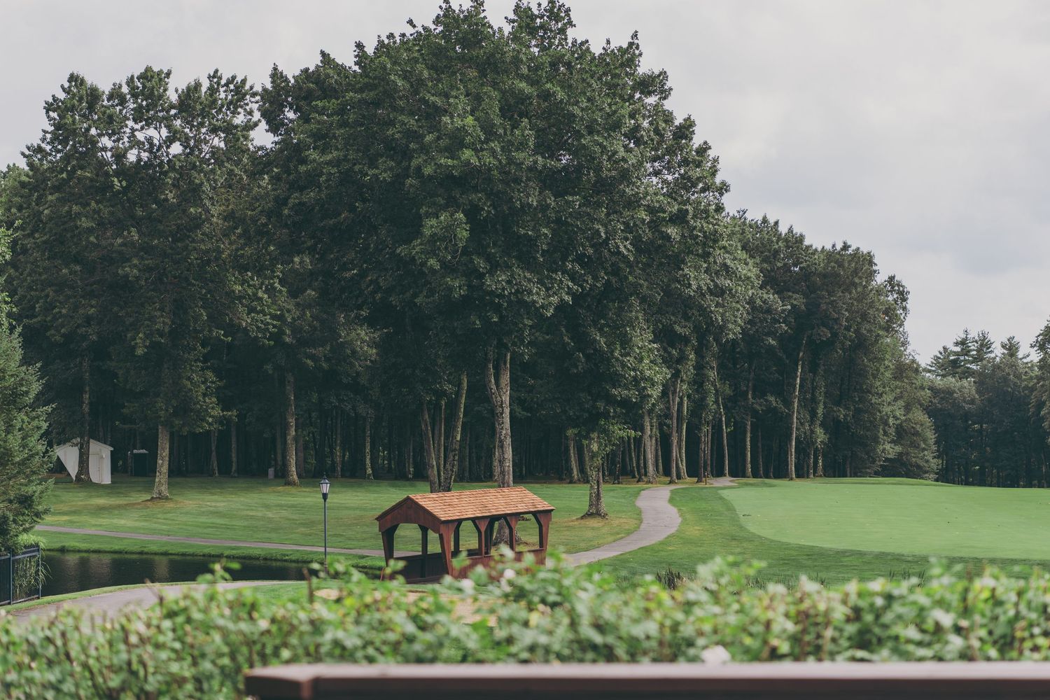 A beautiful green golf course landscape with a rustic shelter house and winding cart path surrounded by trees.