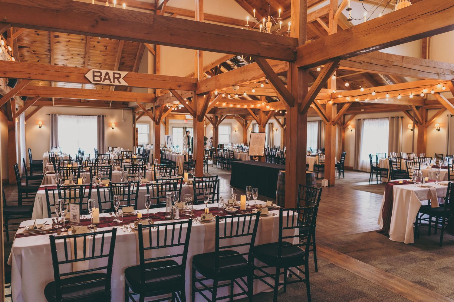 Rustic wood beam event venue interior with black chiavari chairs arranged in neat rows under vaulted ceilings.