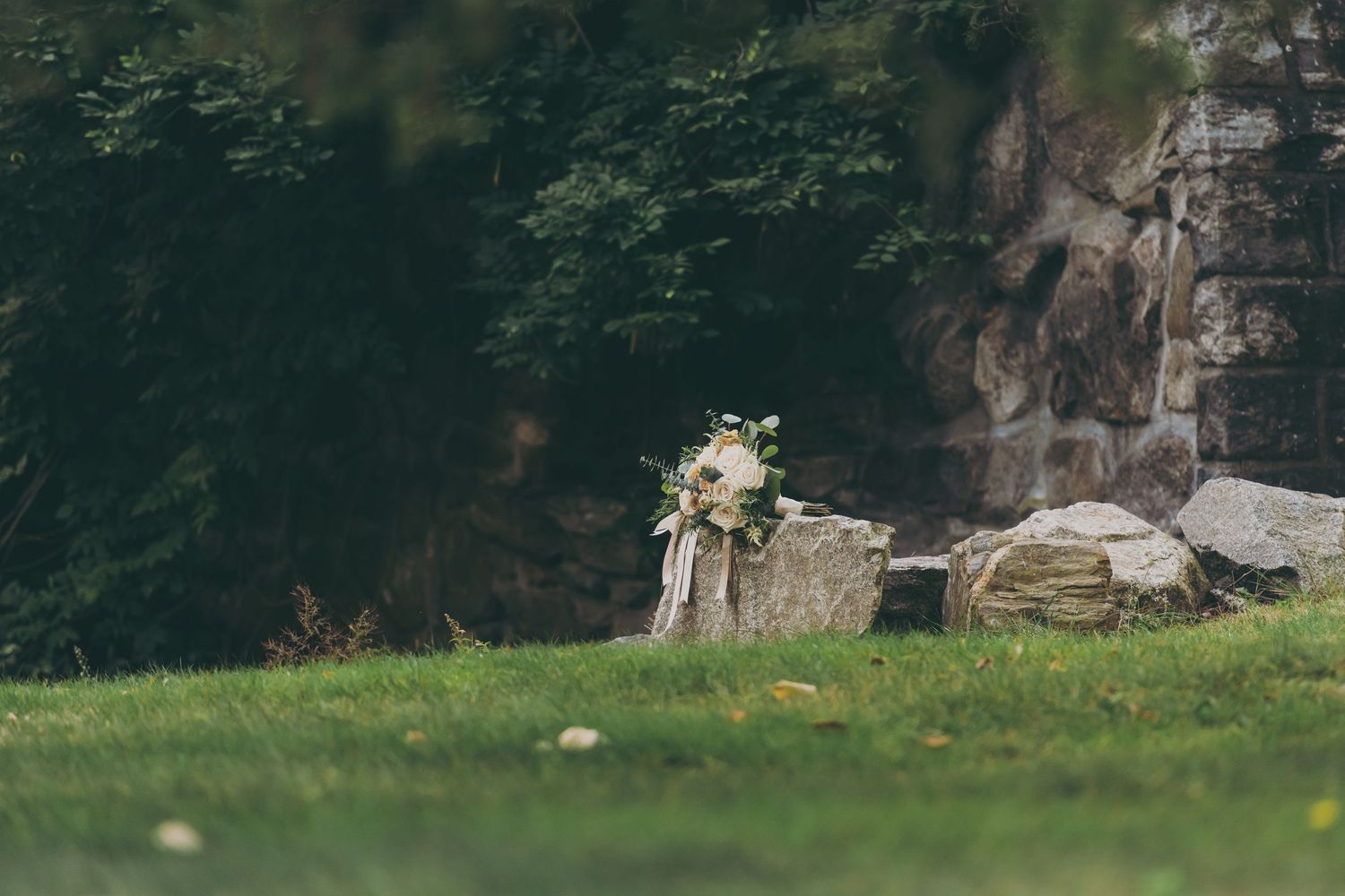 White floral bouquet placed on natural stone wall in garden setting.