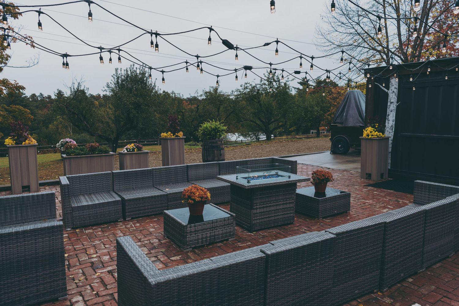 Modern outdoor patio seating area with grey cushions and string lights on brick pavers at dusk.