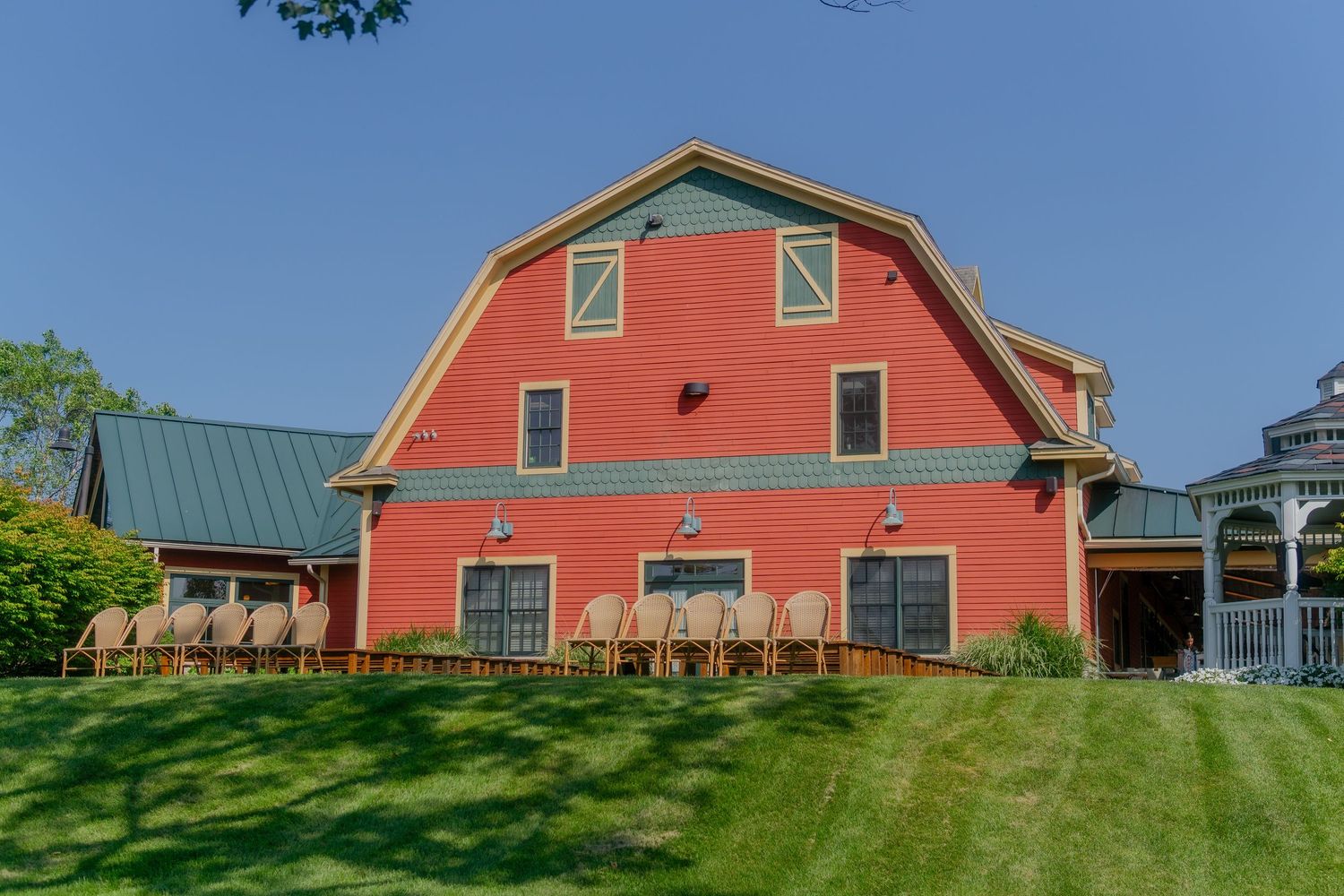A bright red barn-style building with green metal roof sits on a manicured lawn with a white gazebo on the side.