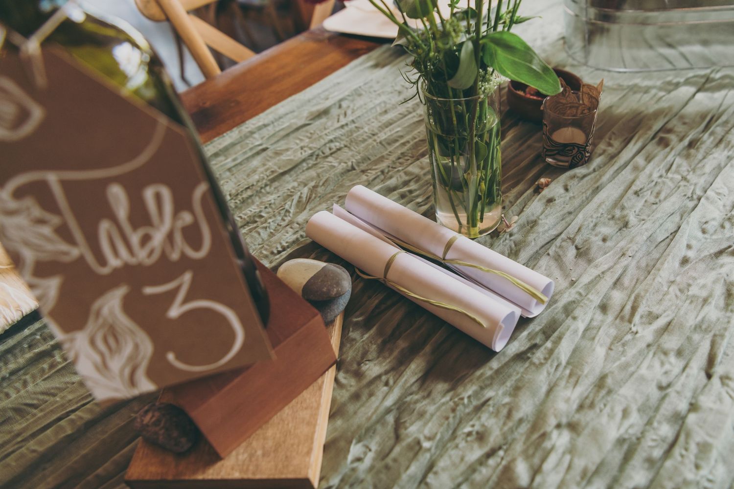 A rustic wooden table decorated with brown paper scrolls, greenery, and vintage-style writing materials sets a romantic mood.