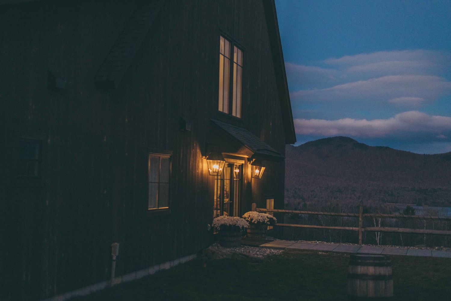 A cozy cabin with warm porch light glows at dusk against a mountain landscape backdrop.