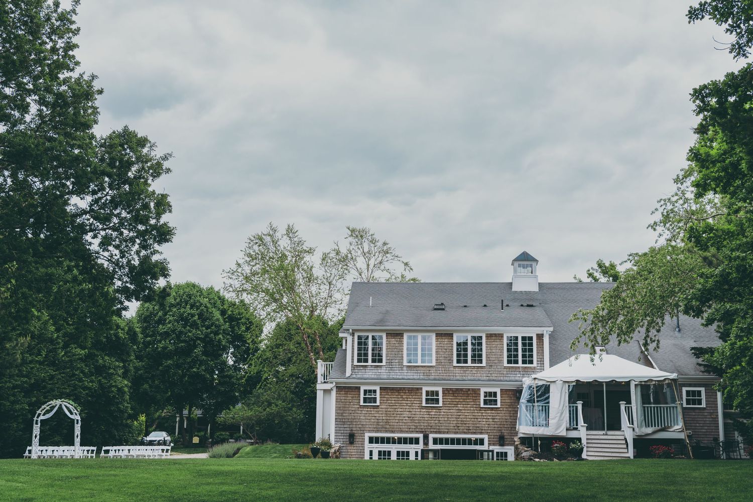 Large colonial style estate with gray siding, dormers, and white gazebo on sprawling green lawn.