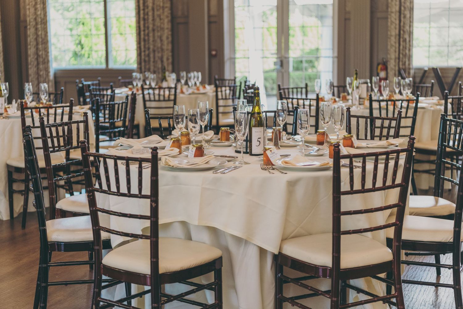 Reception hall set up with elegant round tables and dark Chiavari chairs for a formal dining event.