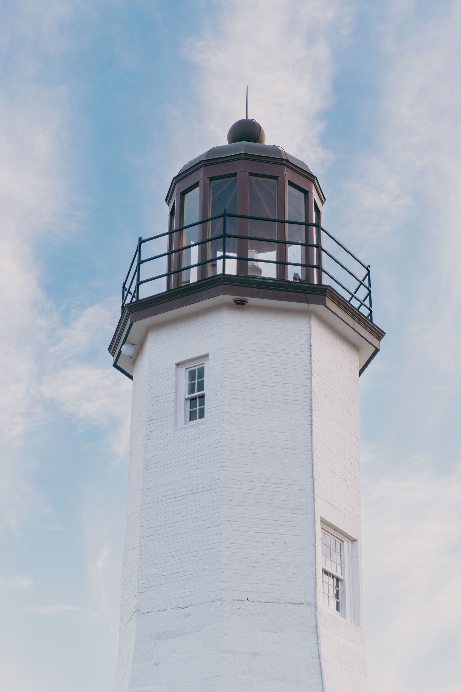 A white lighthouse tower with a domed lantern room against a blue cloudy sky.