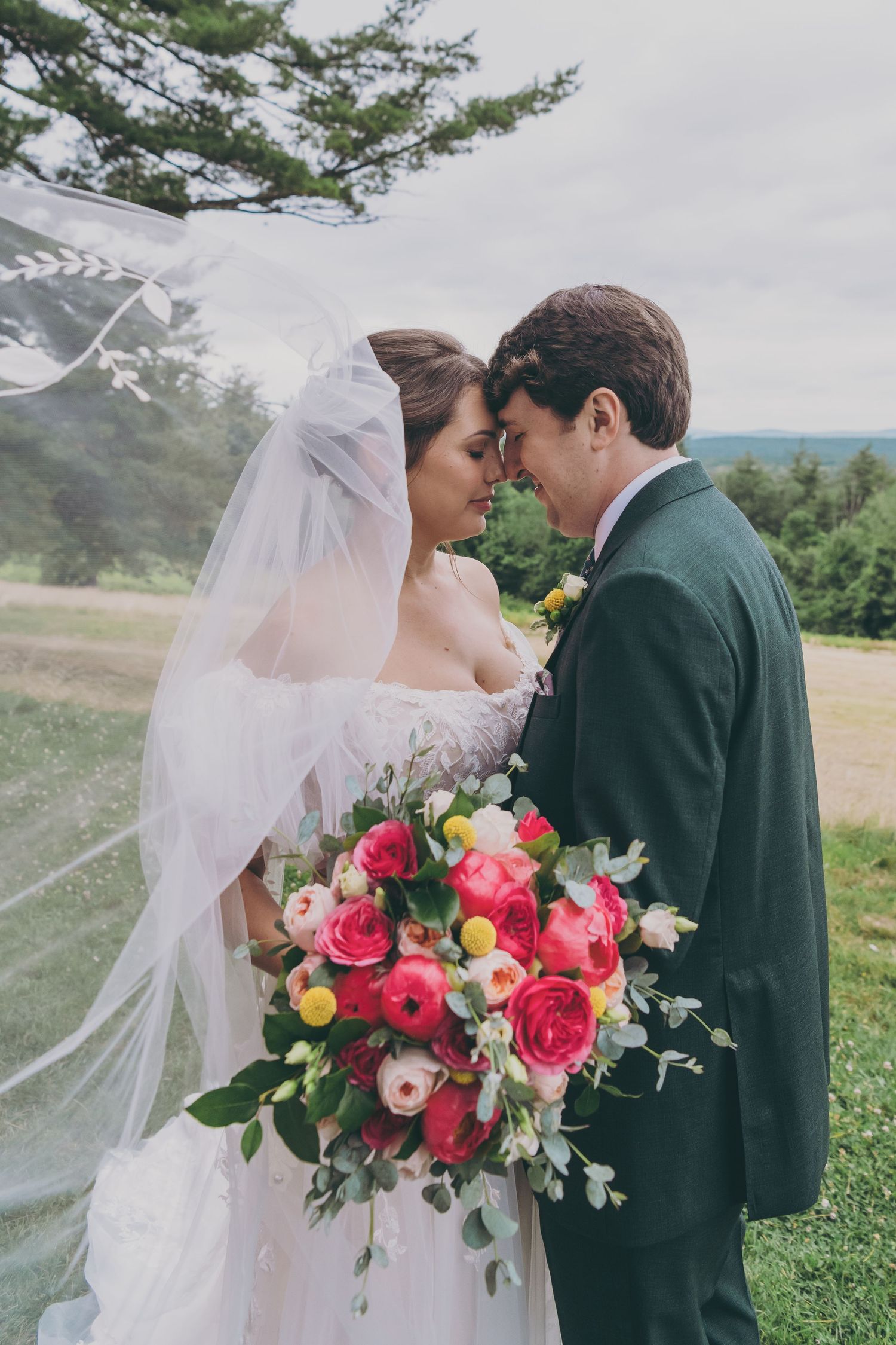 Romantic wedding portrait outdoors with stunning mountain view and vibrant pink bouquet.