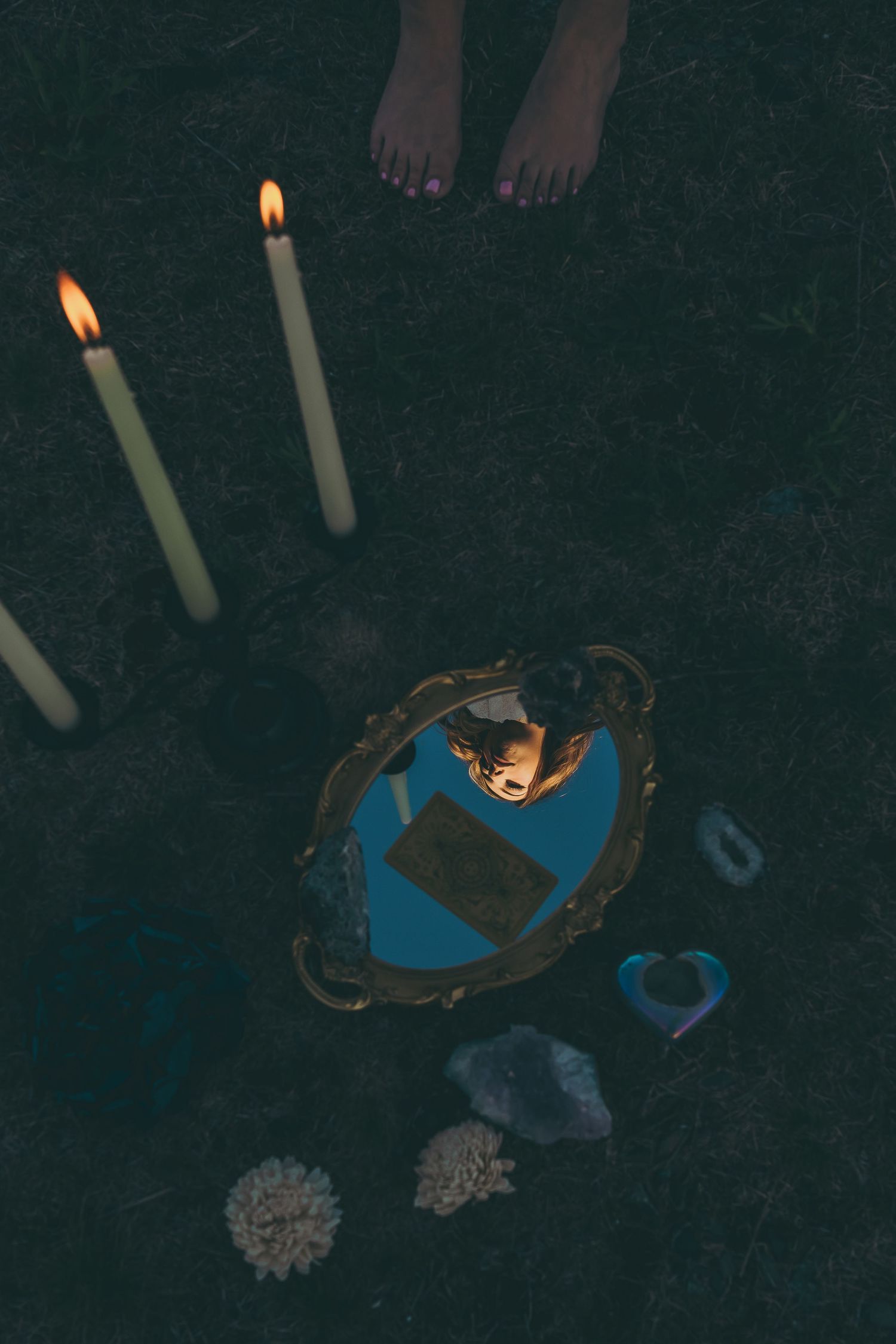 Mystical still life with lit candles, mirror and crystals on dark surface.