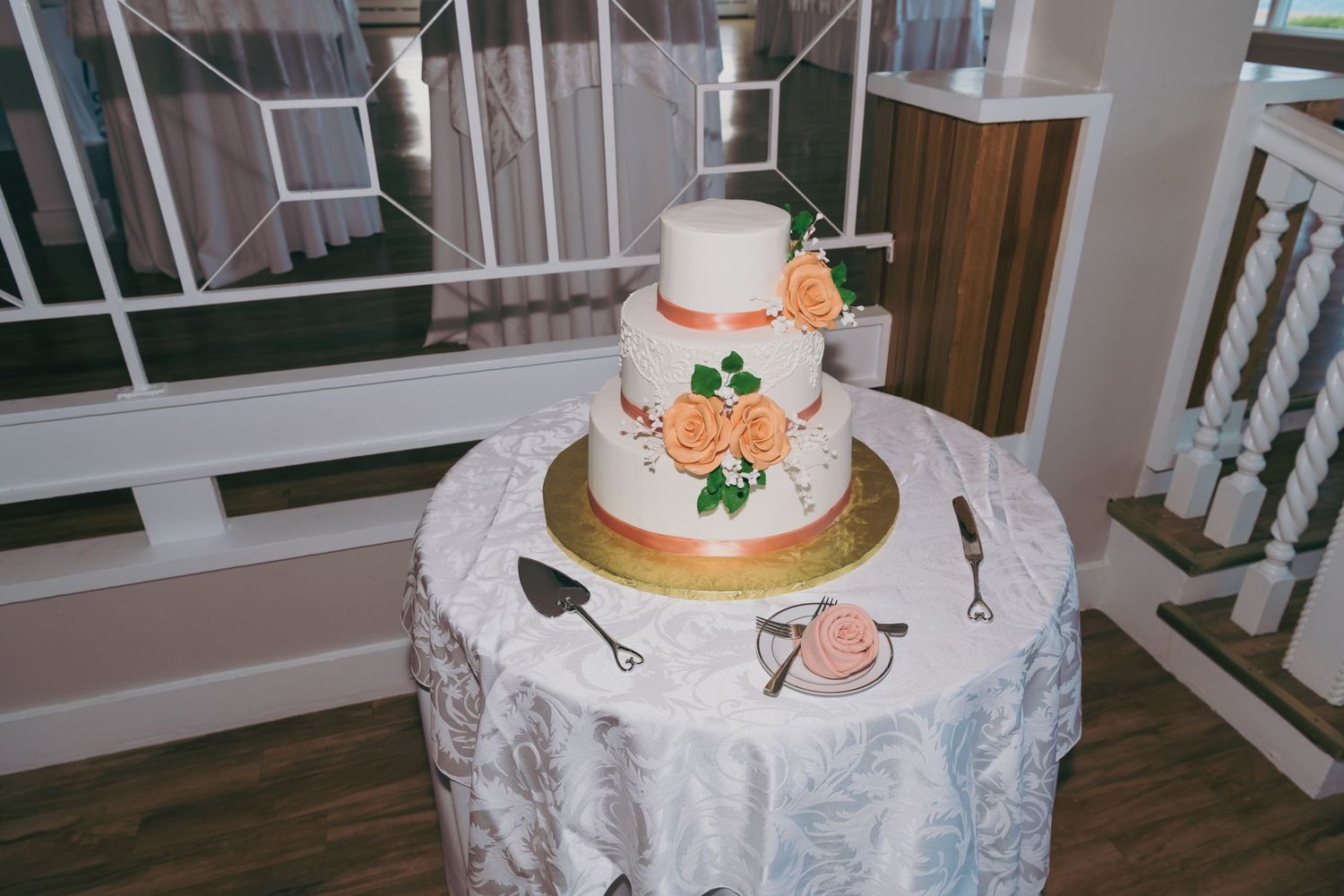 Three elegant white wedding cakes with floral decorations displayed on lace-covered tables at an indoor venue.