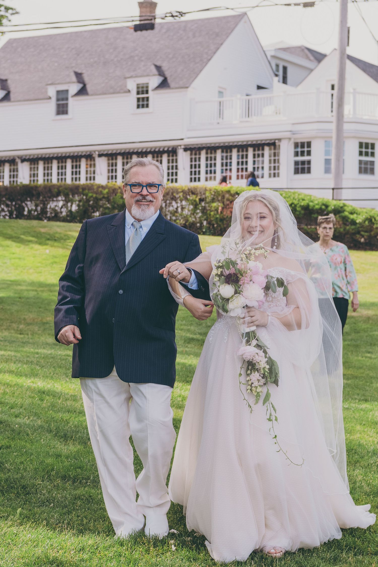 Wedding ceremony at a grand white house with manicured lawn and beautiful landscaping on a sunny day.