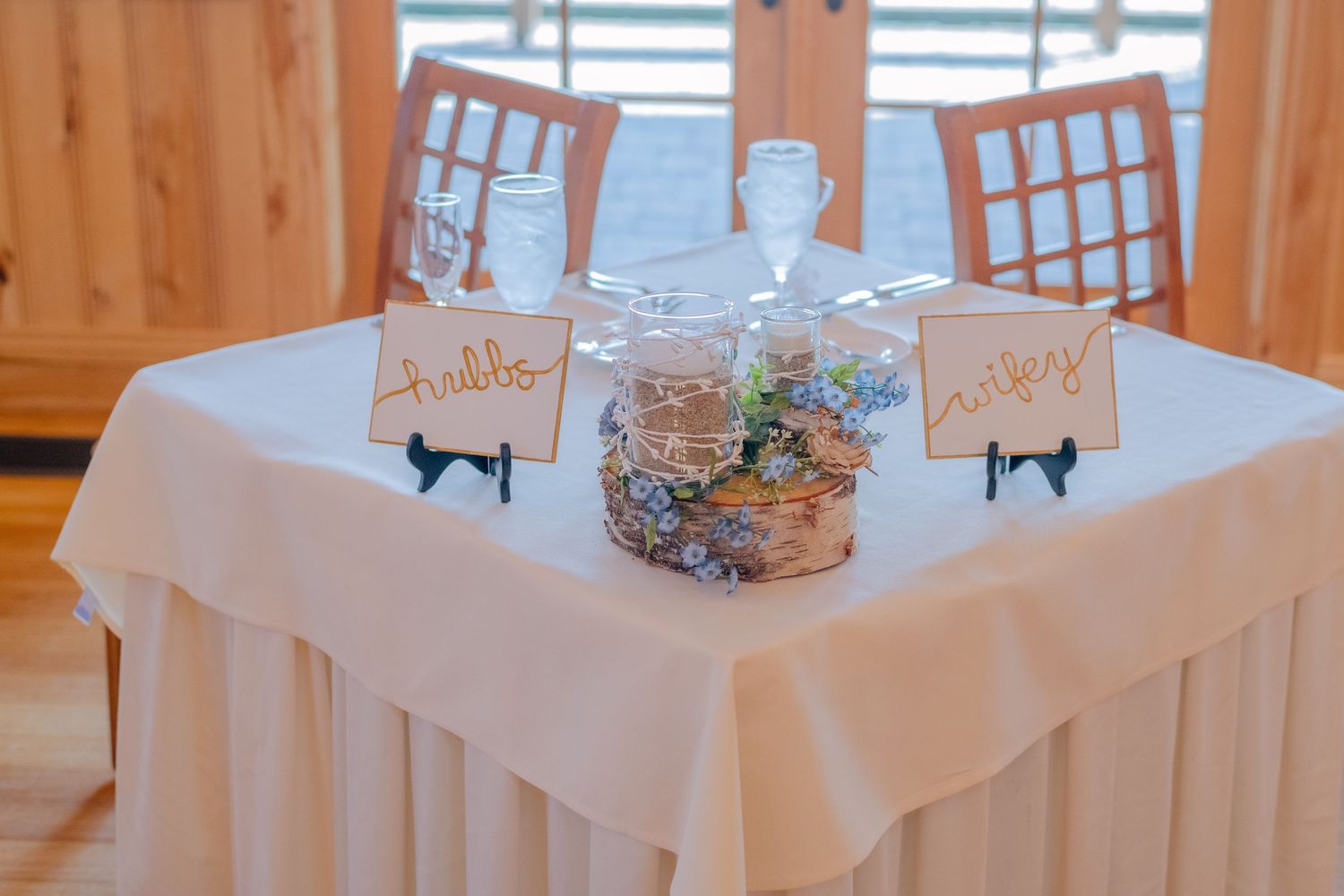 A romantic sweetheart table setup with white linens, chiavari chairs, and decorative name cards for a wedding reception.