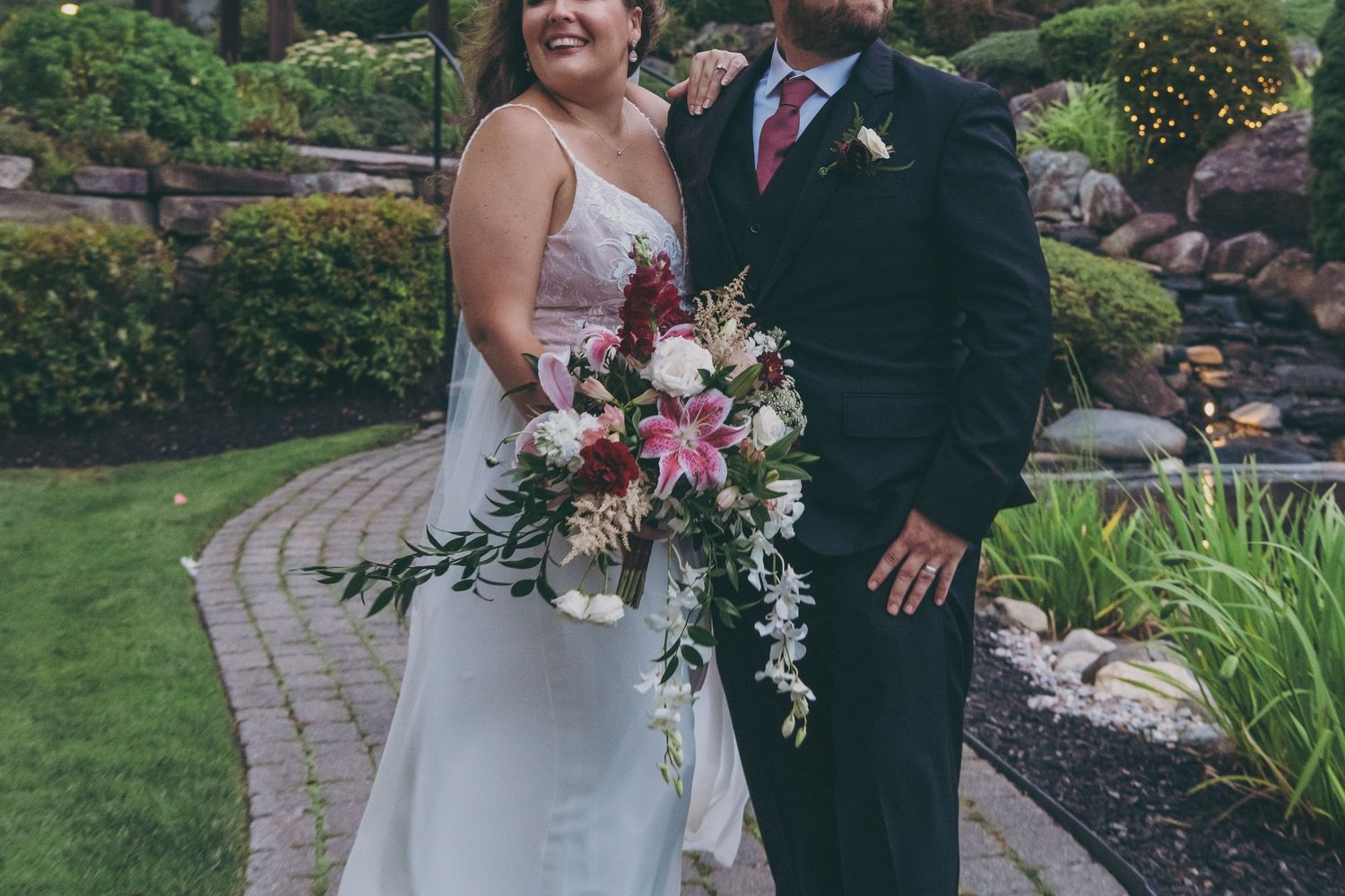 Wedding couple stands on garden pathway with beautiful landscaping and stonework.