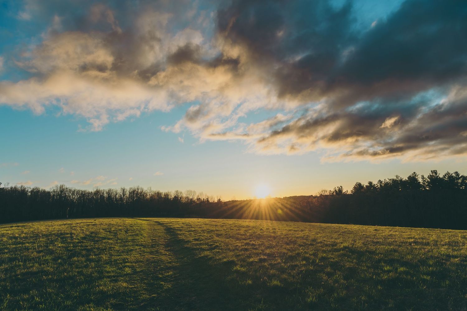 Panoramic sunset landscape over rolling hills with dramatic clouds and golden sunbeams.
