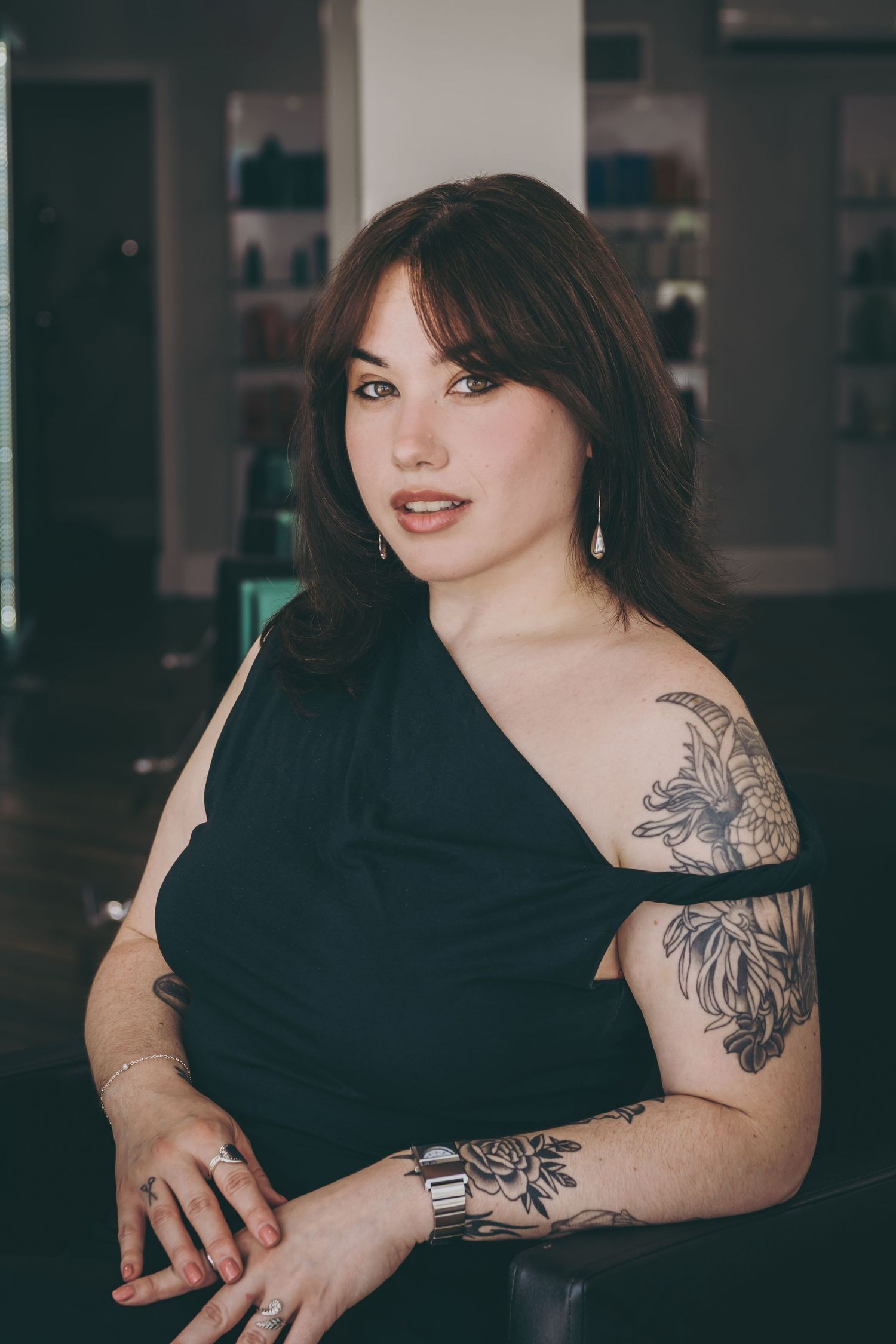 Portrait showing floral arm tattoos and black dress in modern studio setting.