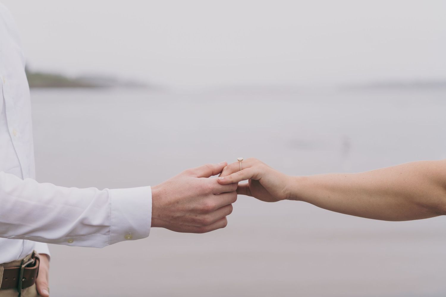 Two hands reaching toward each other exchanging a business card against a light gray background.