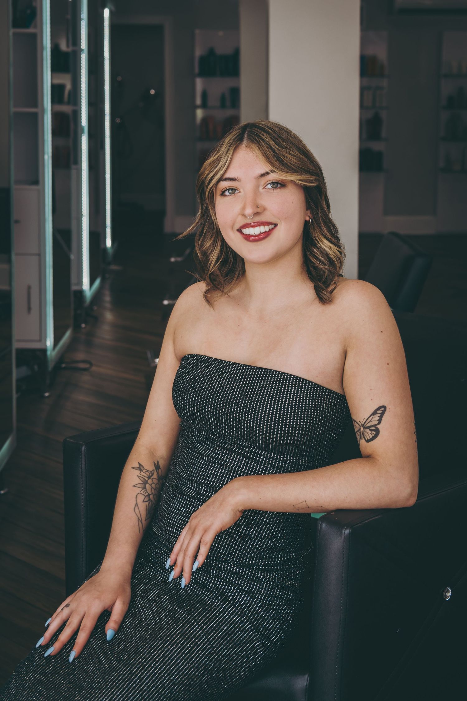 Portrait in black strapless dress showing delicate tattoos in modern studio environment.
