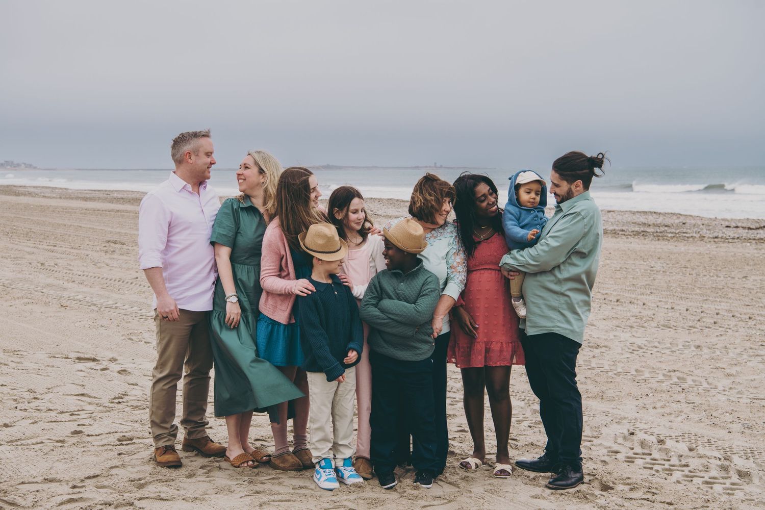 Group of people in coordinated outfits standing together on a sandy beach during an outdoor photo session.
