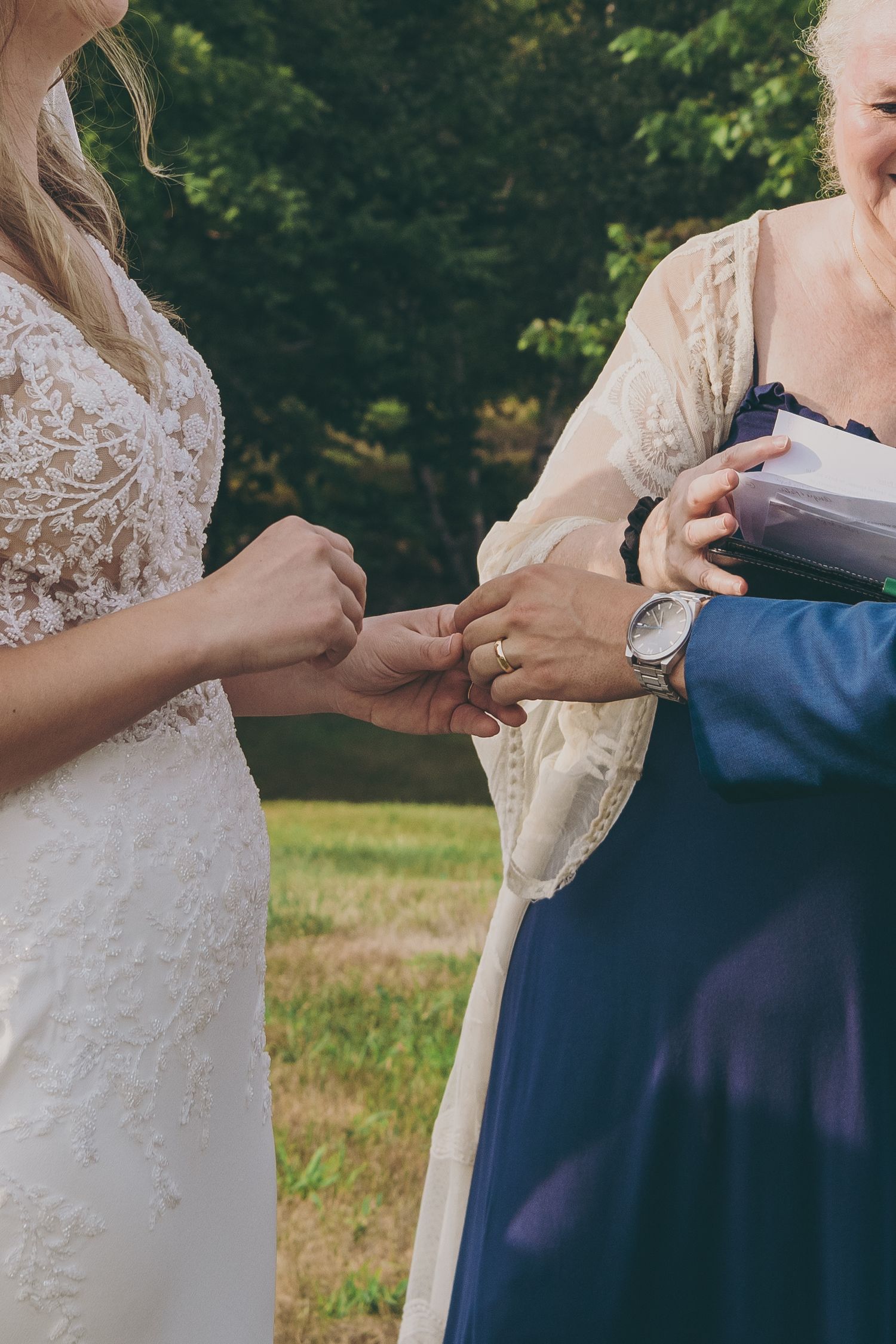 Close-up of hands exchanging rings during wedding ceremony with lace dress details.