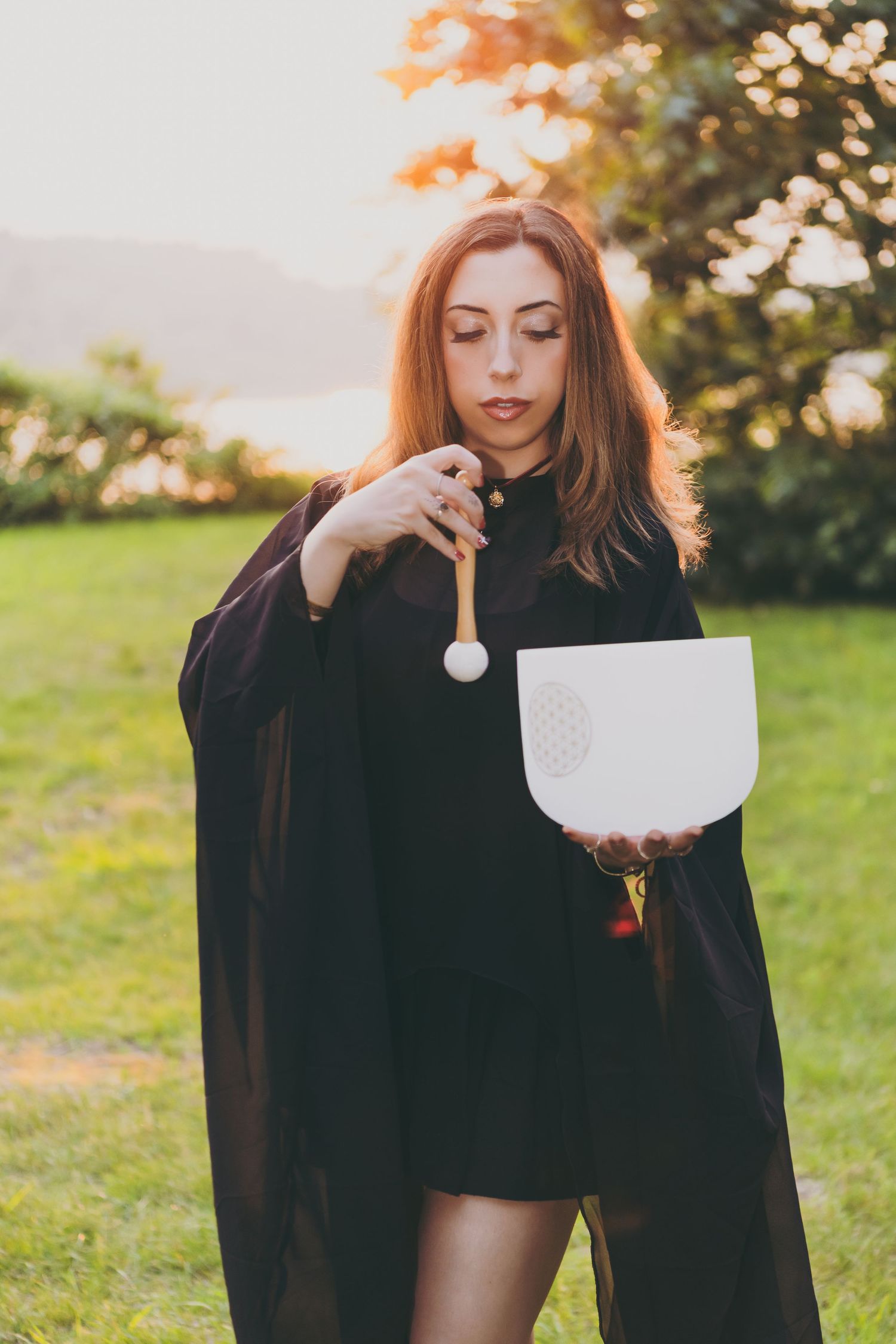 A figure in a dark cloak performs an artistic sequence in a sunlit meadow at golden hour.
