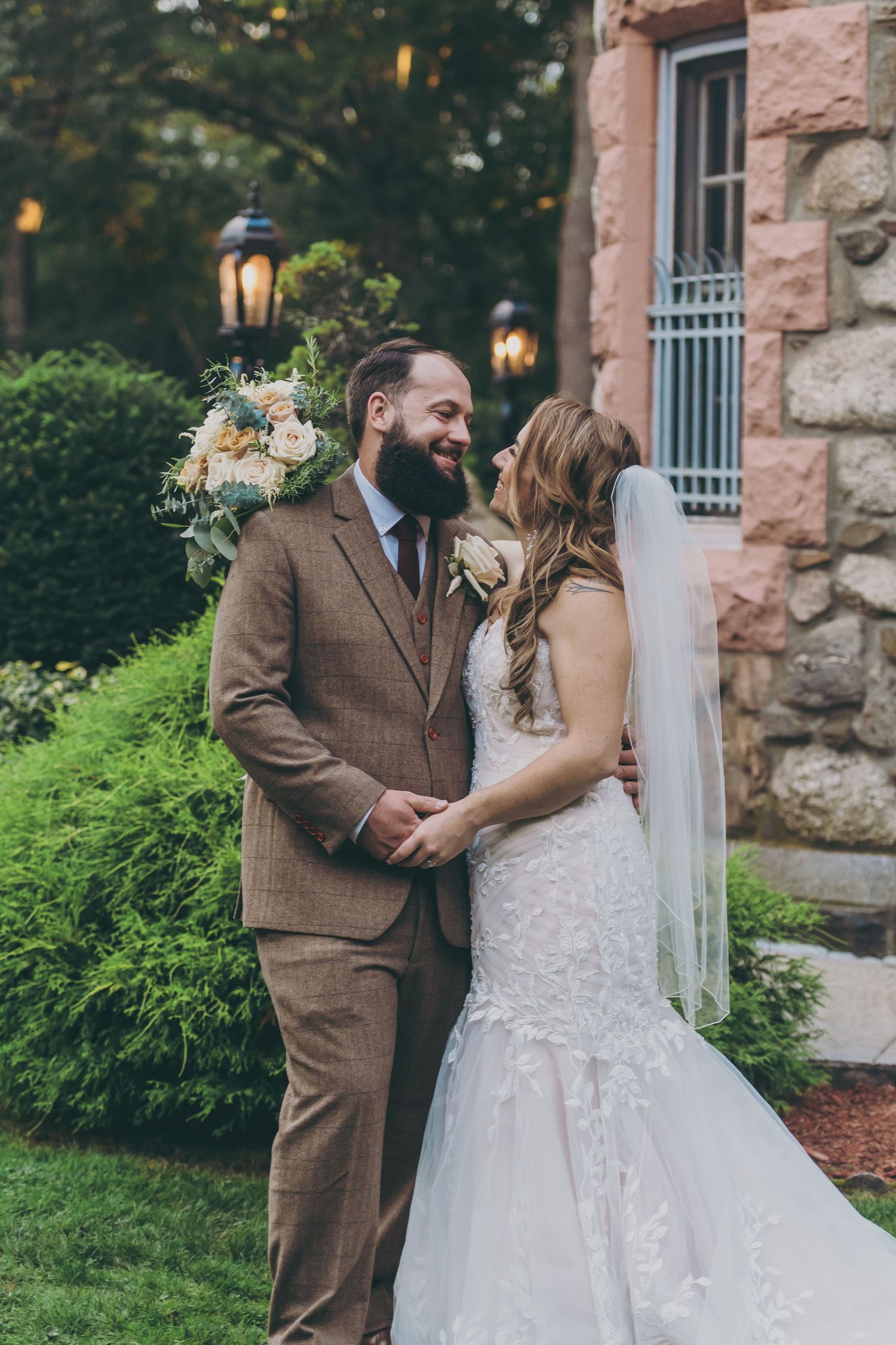 Romantic outdoor wedding scene against pink stone wall with lush greenery and lantern lighting.