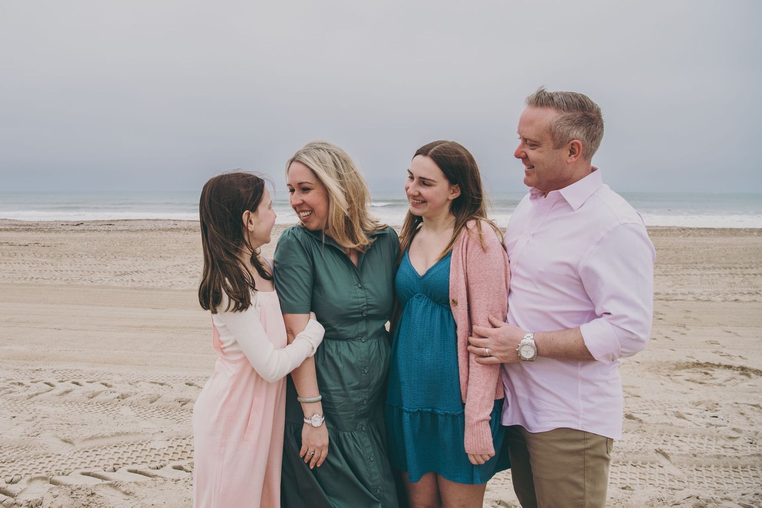 A group of friends share joyful laughter together while standing on a cloudy beach in casual attire.