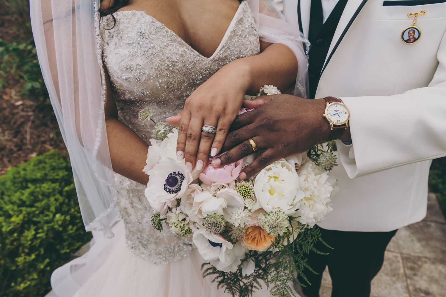 Newlywed couple's hands with wedding rings rest on a beautiful bouquet of white and pink flowers.