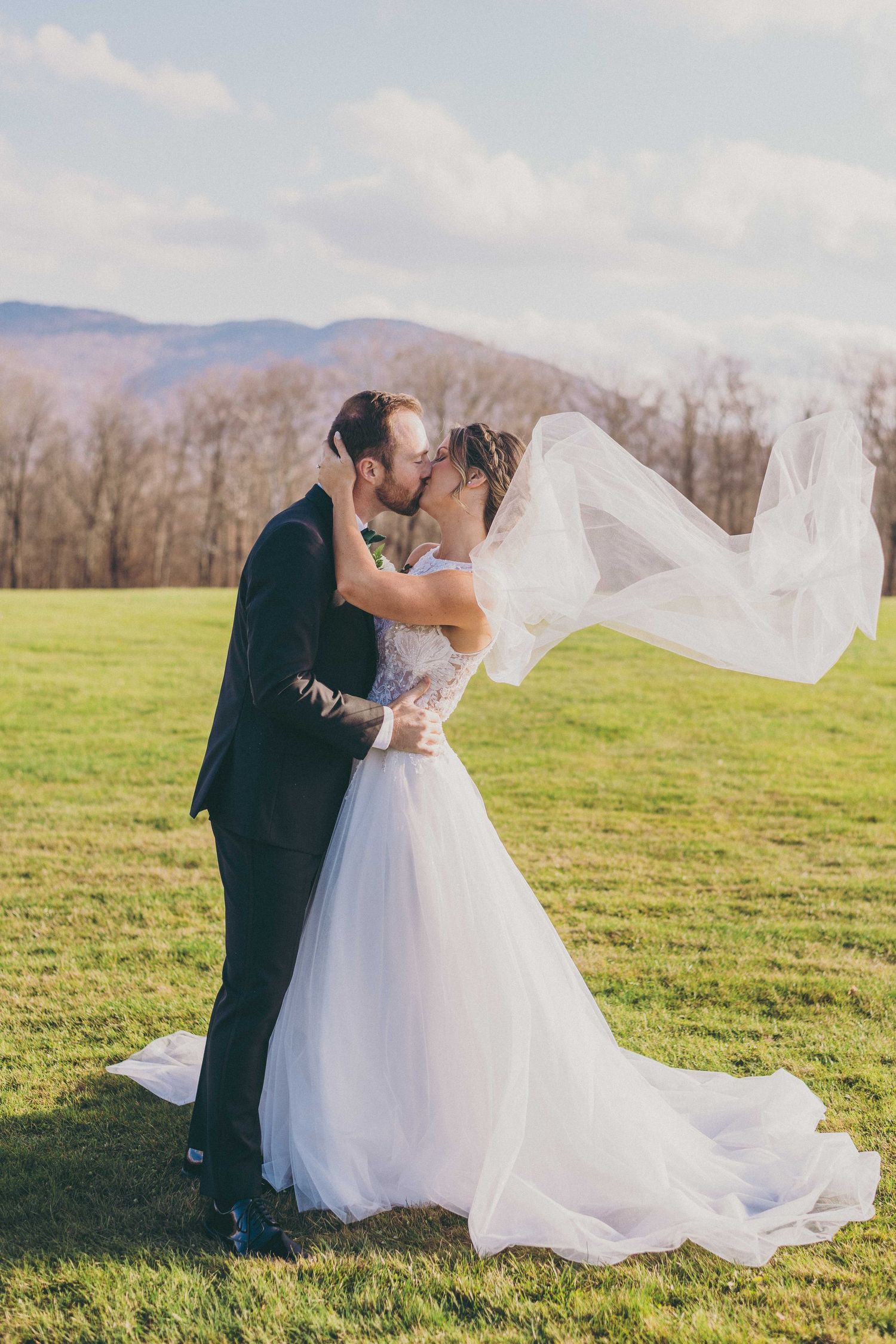 A romantic wedding couple shares an intimate moment in a sunlit meadow as the bride's veil flows in the breeze.