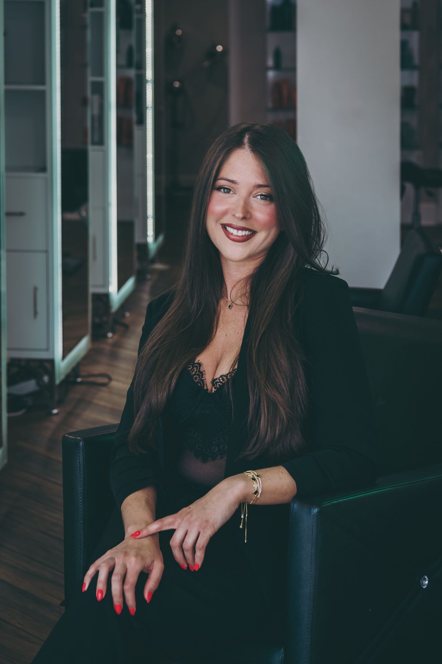 Portrait of woman in black top seated in modern salon with sleek interior lighting.