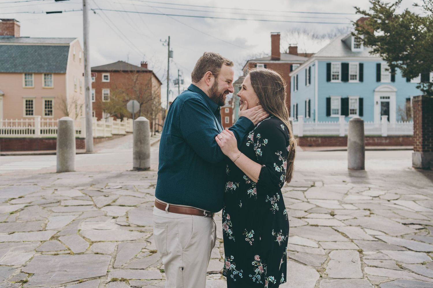 A couple embraces on a stone patio with historic buildings in the background.