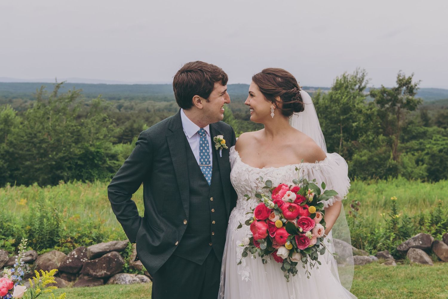 Elegant outdoor wedding portrait with sweeping hillside views and bright floral bouquet.