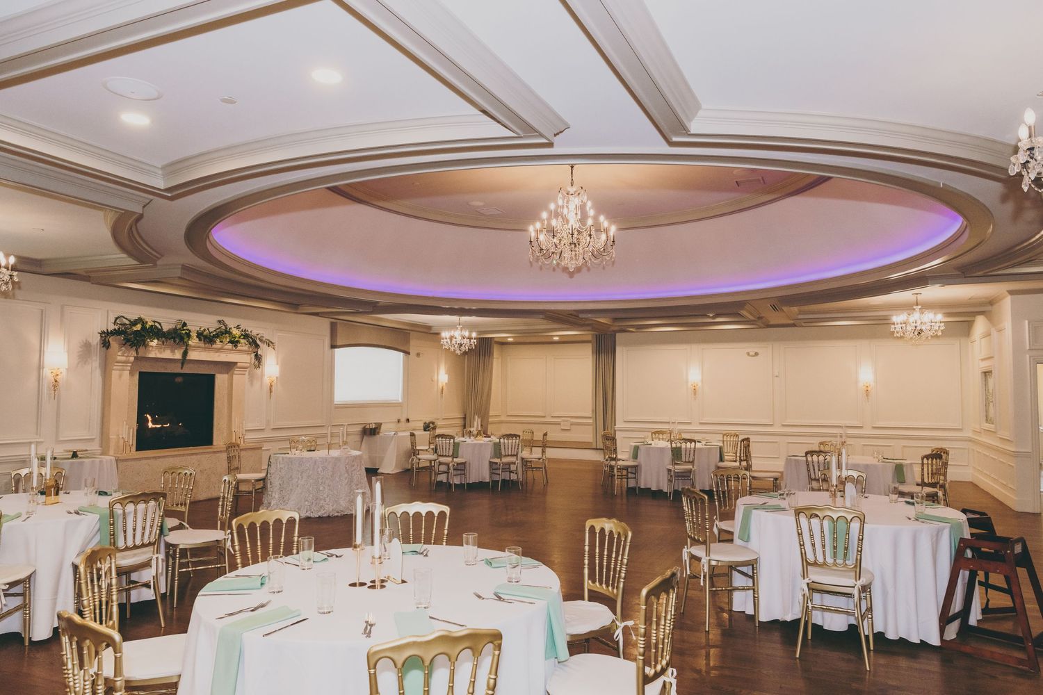 Elegant white banquet hall with ornate ceiling details, crystal chandeliers and cream-colored chairs set for formal events.