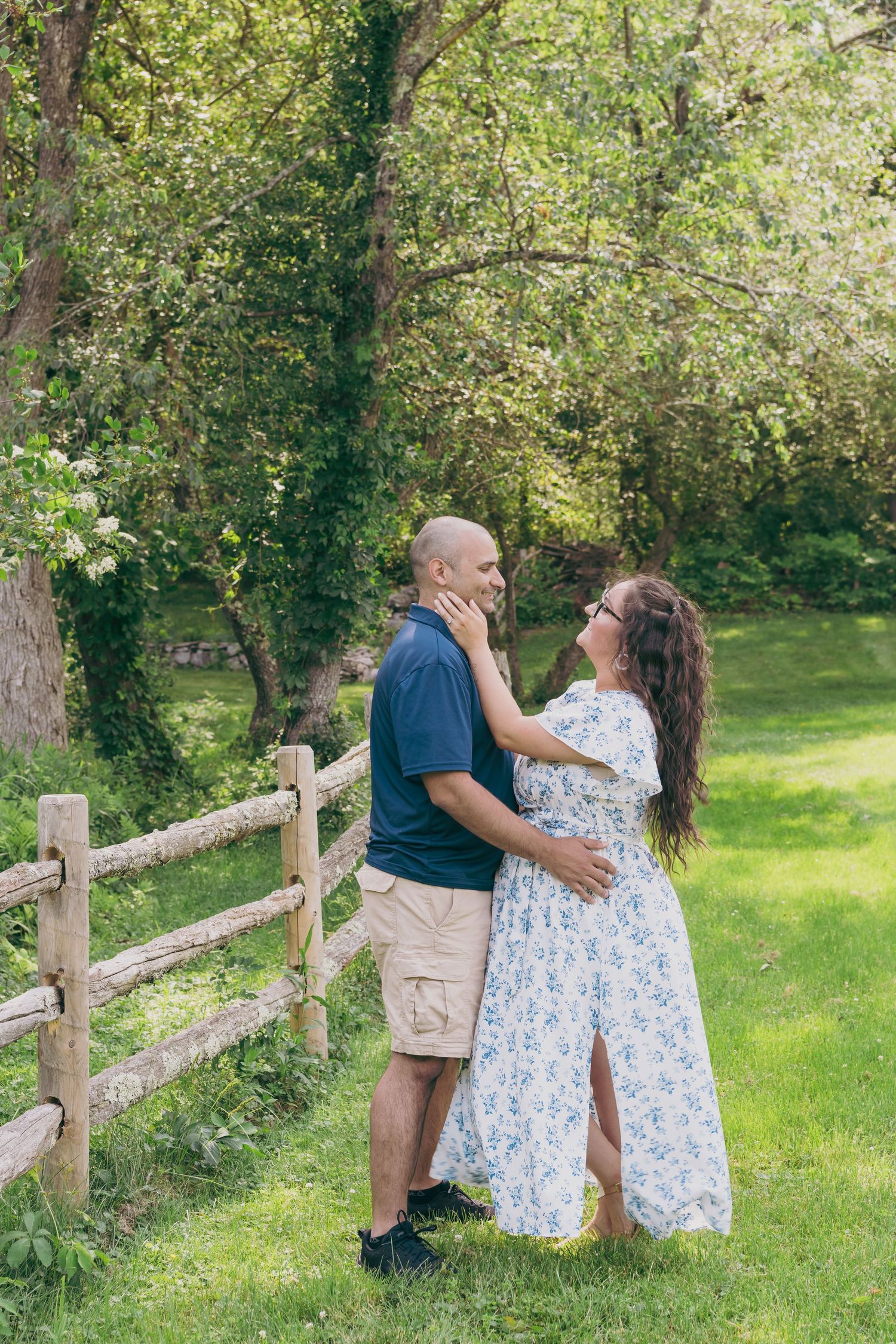 A couple shares a romantic moment by a wooden fence in a sunlit conservation area.