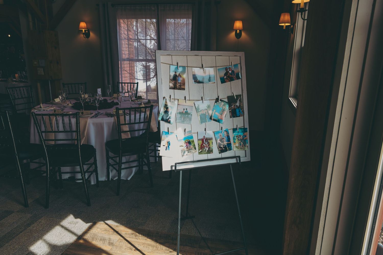 A photo display board with snapshots stands in a dimly lit restaurant dining room with wooden chairs and wall sconces.