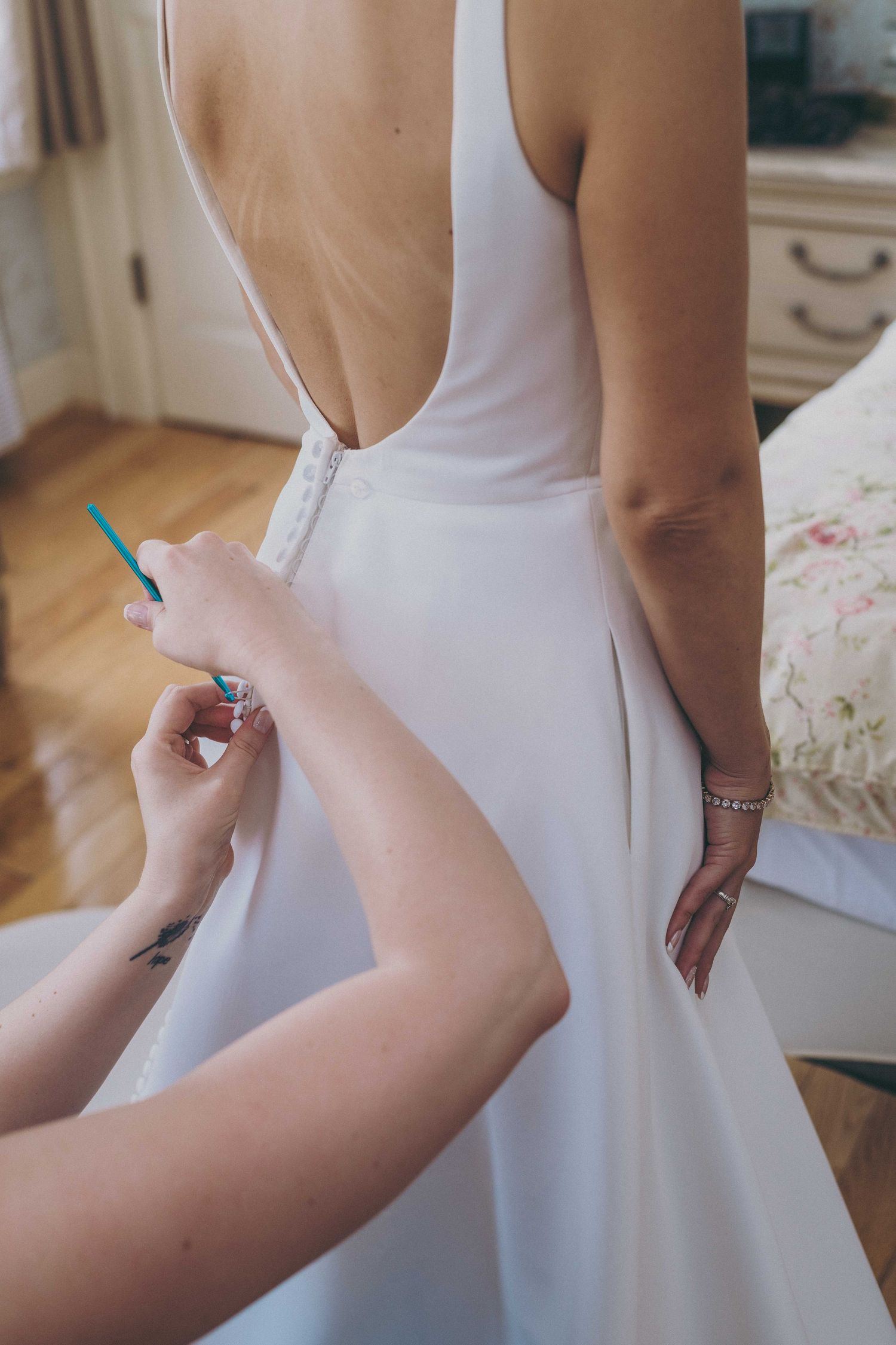 Close-up shot of someone zipping up a white wedding dress with an open back design.