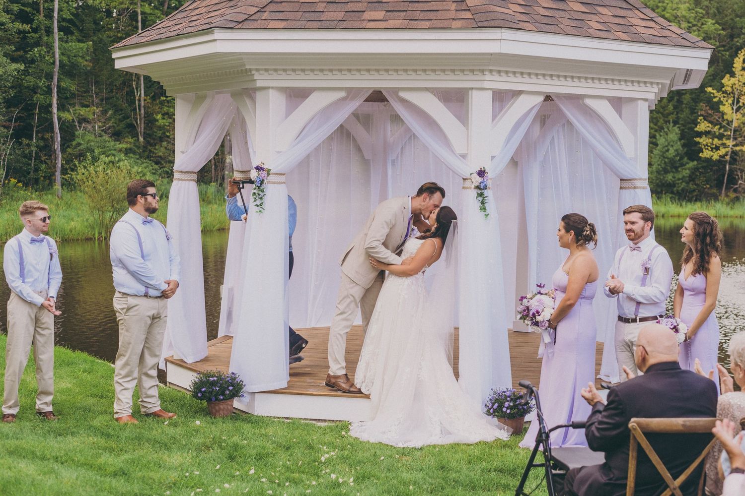 A couple shares an intimate moment during their wedding ceremony in a white garden gazebo on a grassy lawn.