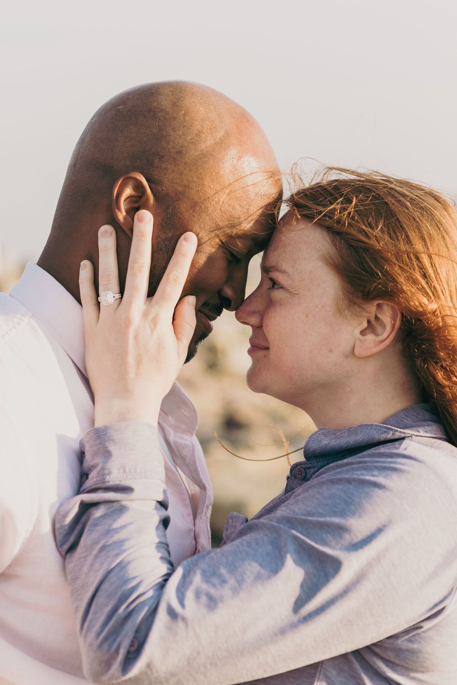 A tender romantic moment between an interracial couple touching foreheads in warm sunlight.