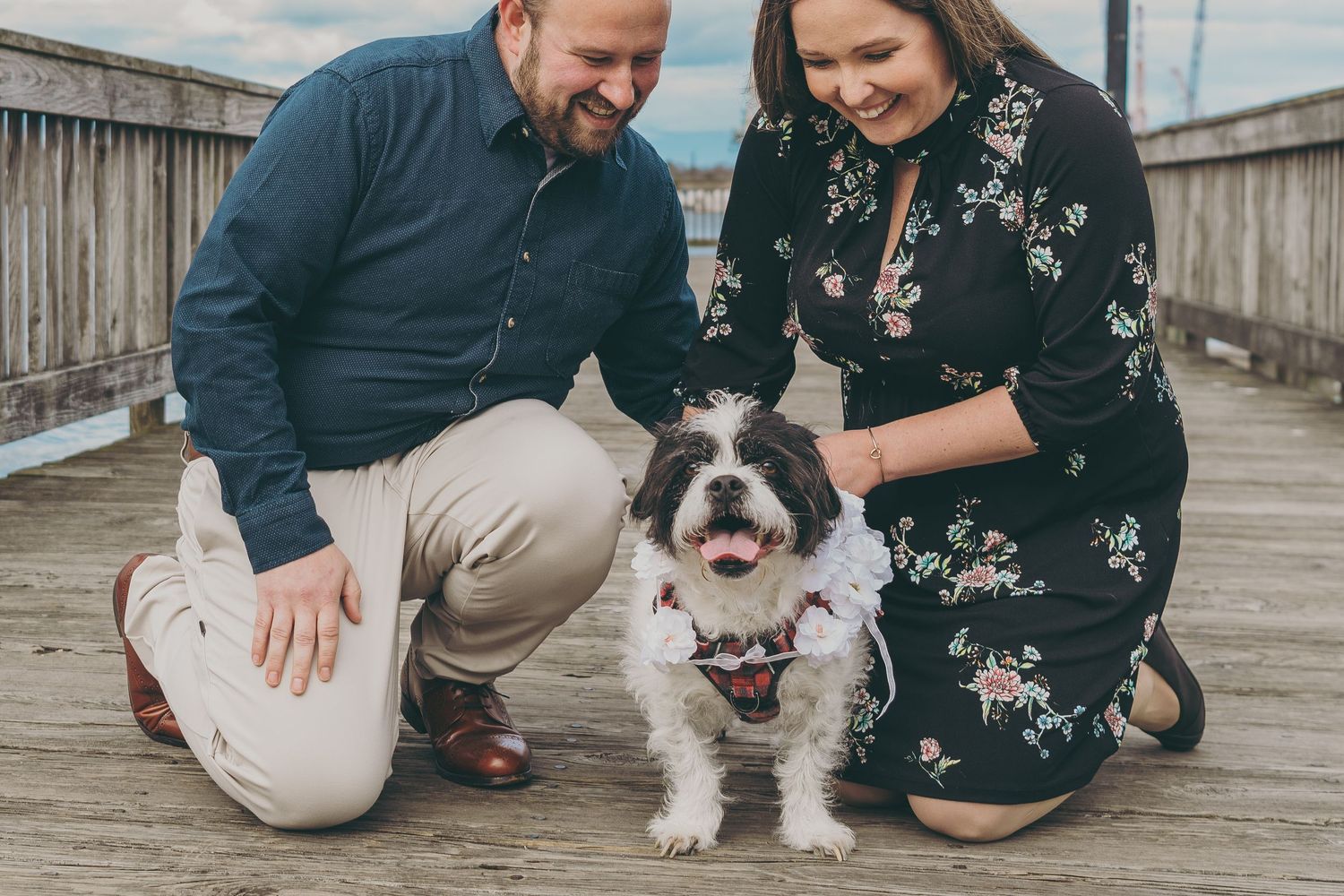 A couple and their small dog sharing a playful moment together on a wooden deck outdoors.