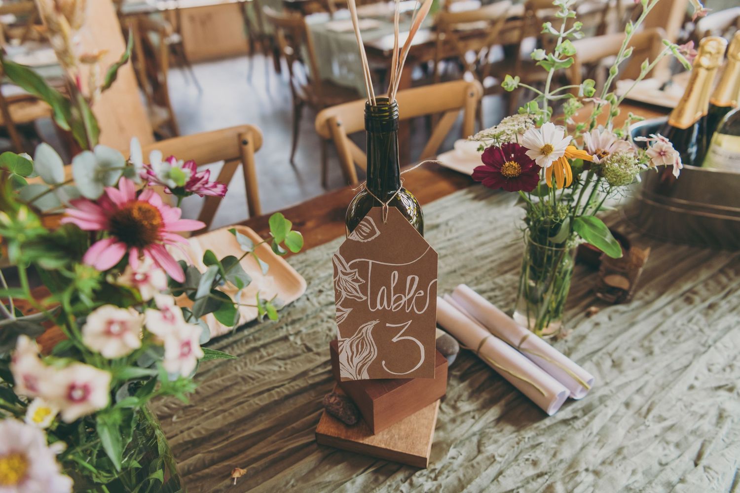 Rustic table setting with colorful floral arrangements and a decorative bottle at a wedding reception.