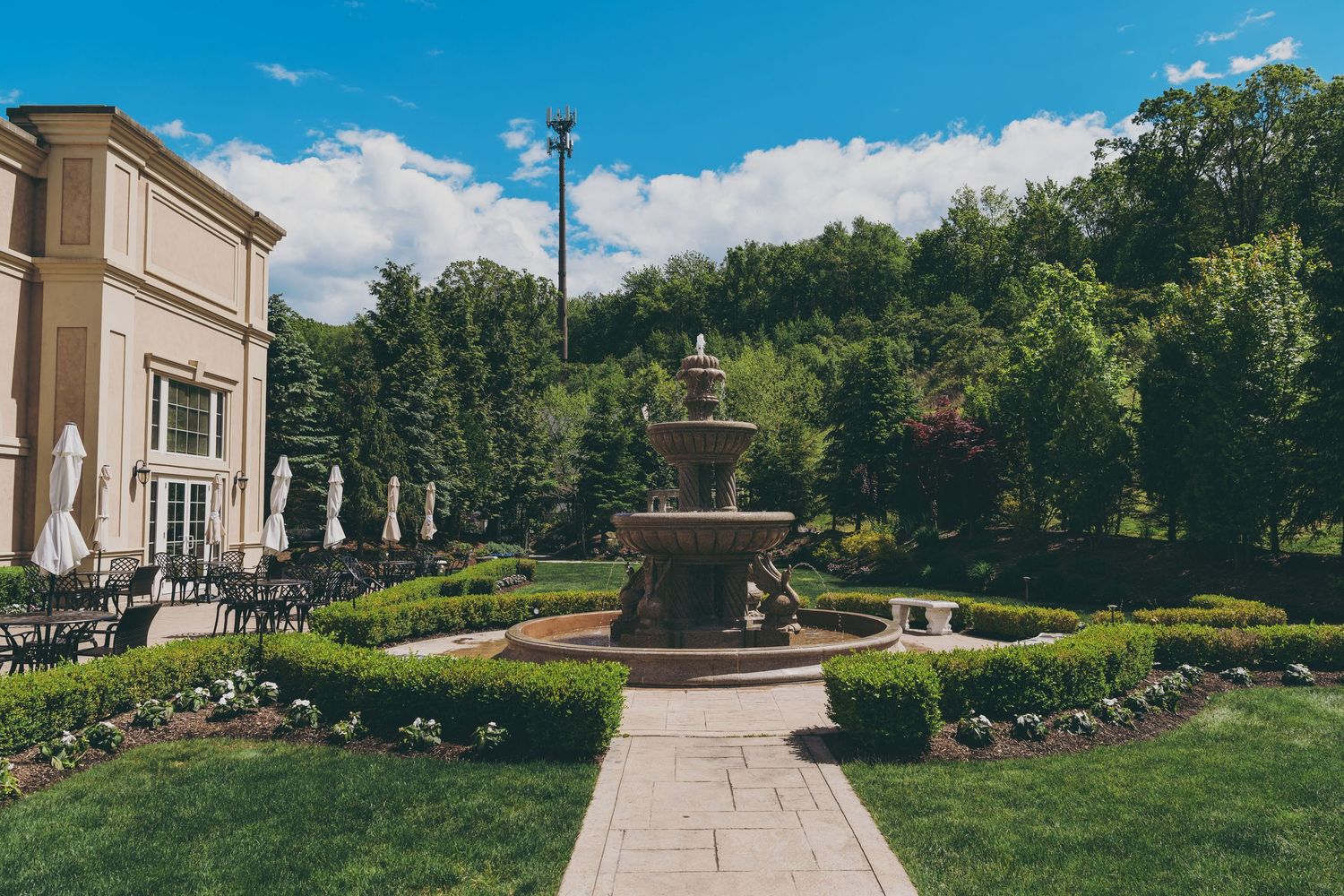 A curved walking path leads up to a grand entrance of an elegant stone building surrounded by manicured gardens.