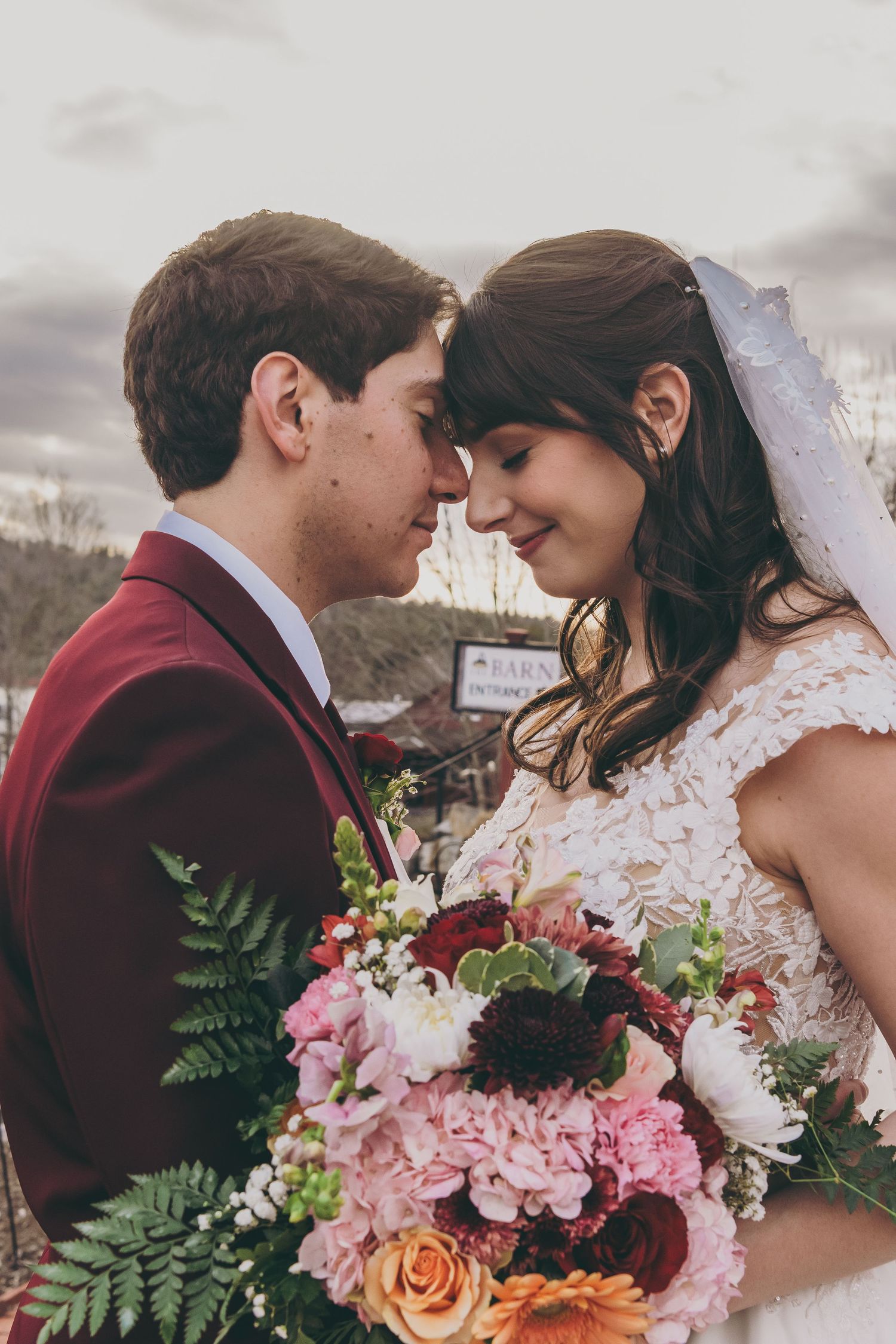 Wedding couple embraces outdoors with a vibrant bouquet of pink and orange flowers.