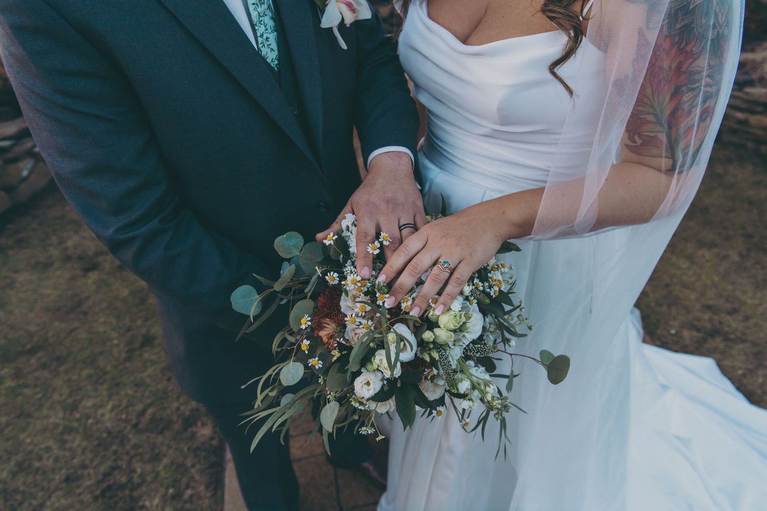 Wedding couple holding white and green floral bouquet against textured stone background.