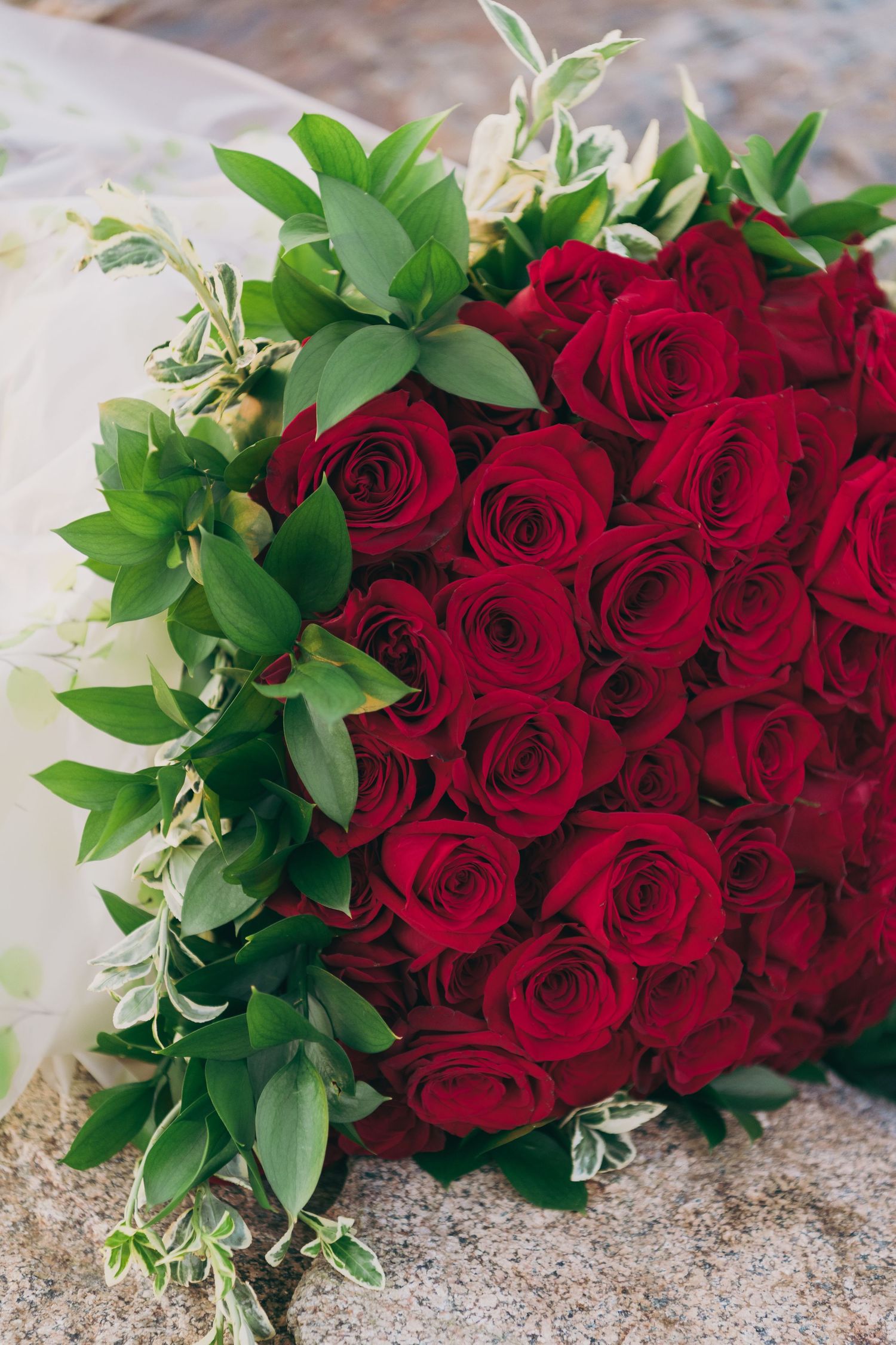 Romantic bouquet of vibrant red roses with green foliage accents photographed on a textured surface.