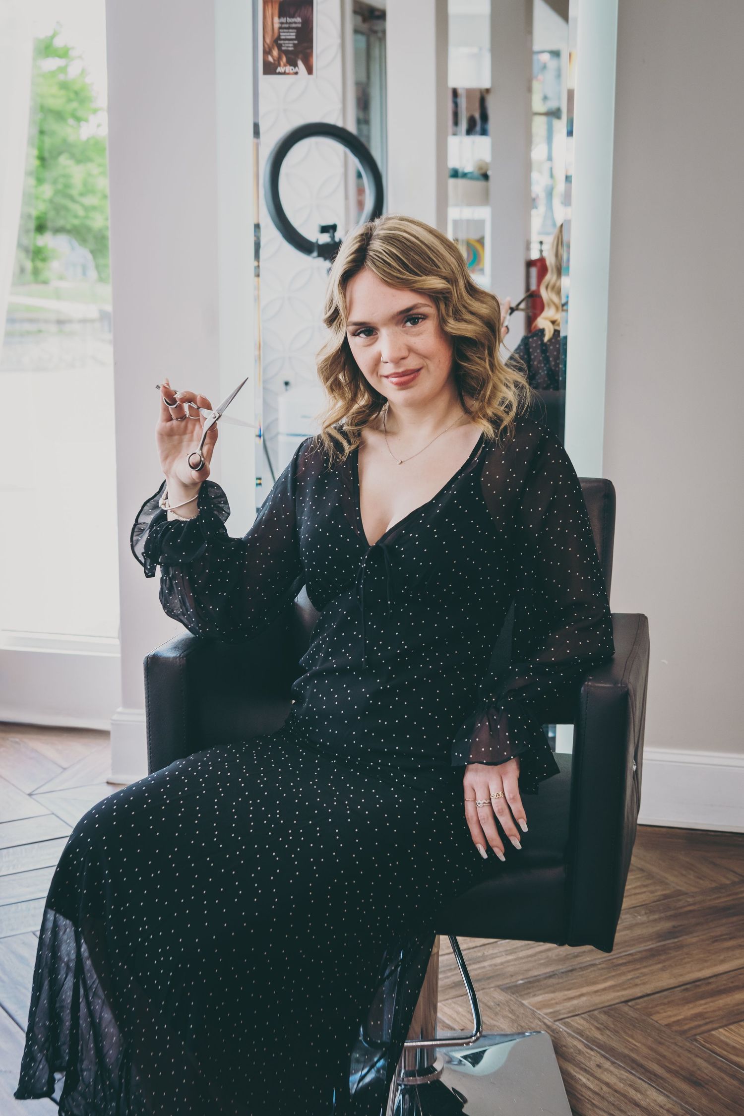 Woman in sparkly black dress poses elegantly in modern interior with hardwood floors.