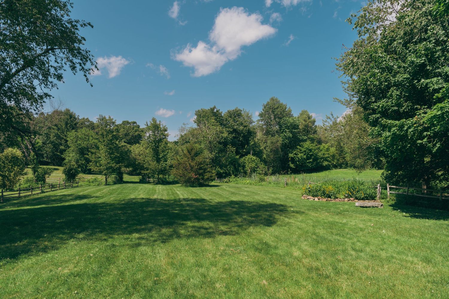 Rolling green hills and trees stretch across a sunny pastoral landscape with blue skies and white clouds.
