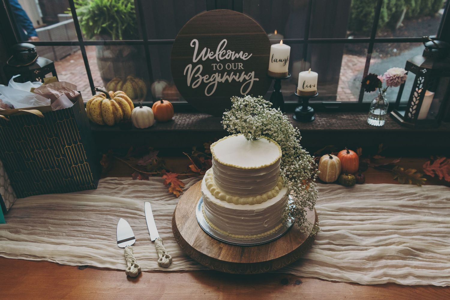 Minimalist white wedding cake decorated with baby's breath on a wooden table with pumpkins and fall decor.