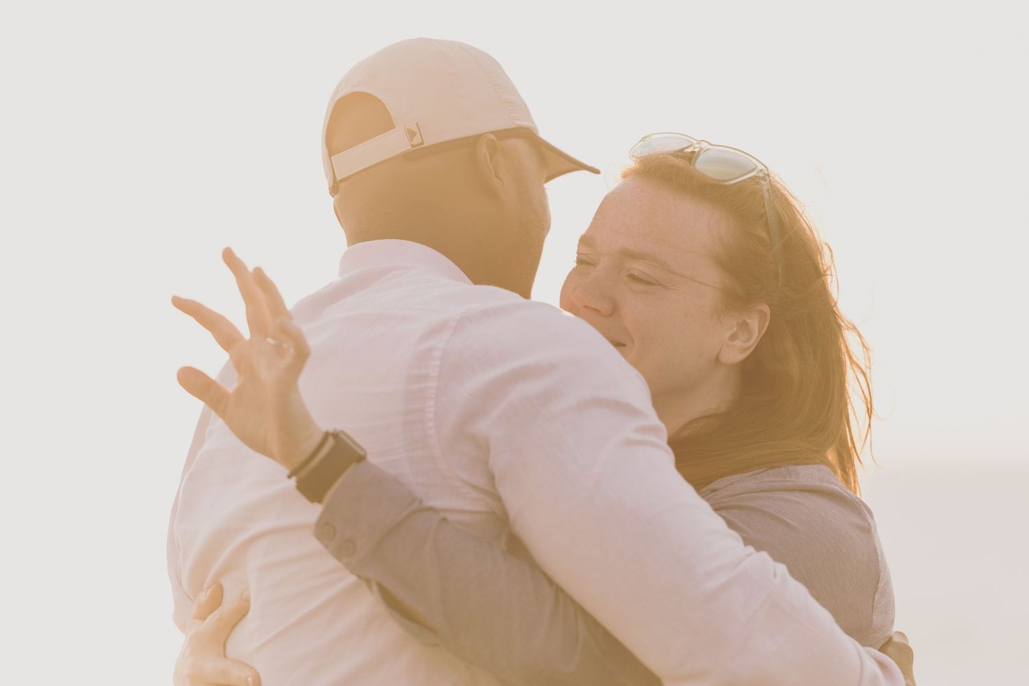 A couple in light-colored clothing dancing together intimately at sunset casting warm silhouettes against the glow.