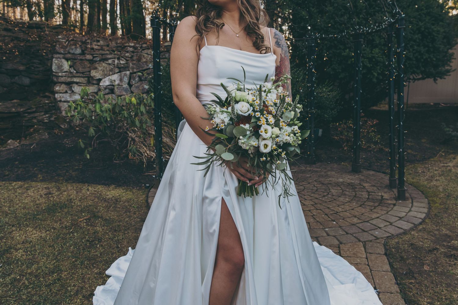 White strapless wedding gown and formal suit details against rustic stone wall backdrop.