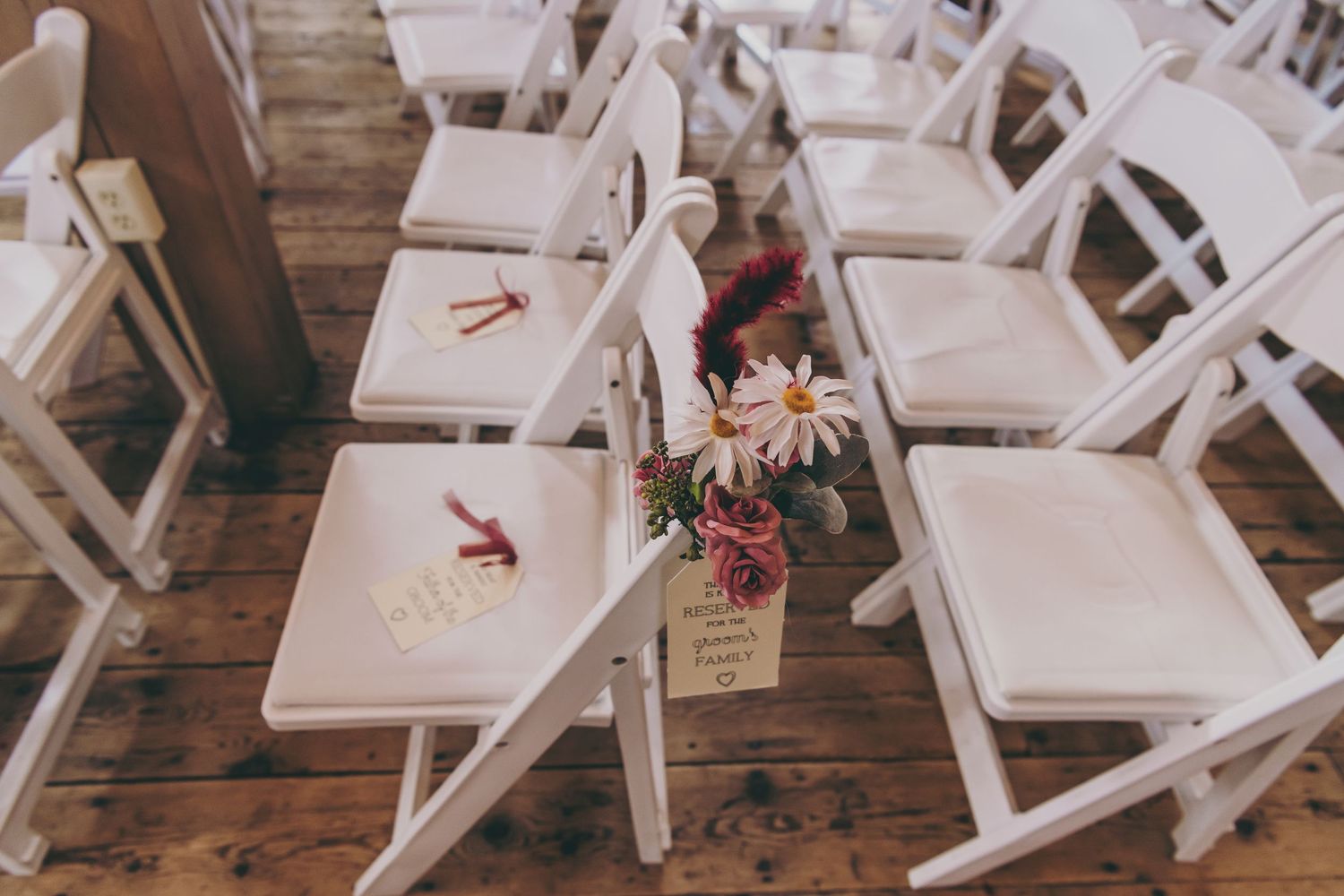 White folding chairs lined up on wooden floors for an indoor wedding ceremony.