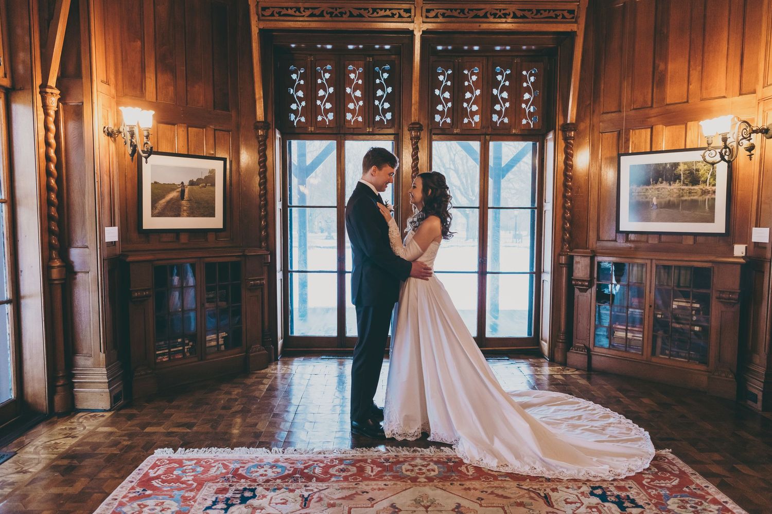 Elegant wooden paneled ballroom interior with ornate details and windows illuminated by warm lighting.